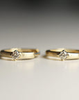 Two small gold hoop earrings with a brushed finish and a single square-set diamond on each lie upright on a white surface.