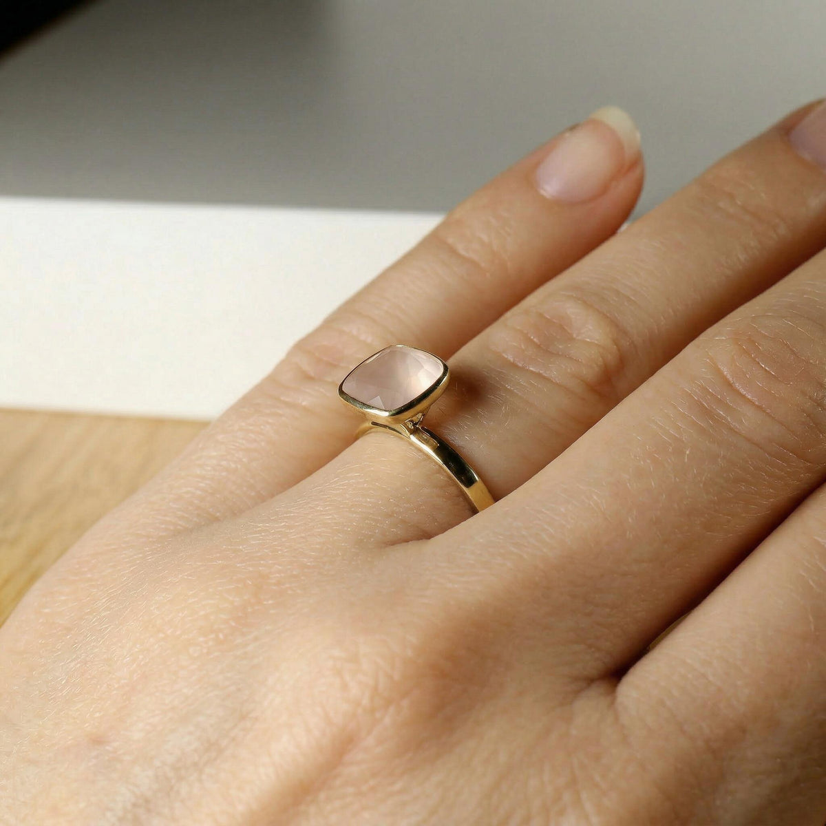 A gold cushion-cut pink gemstone ring worn on a finger, viewed from the side.