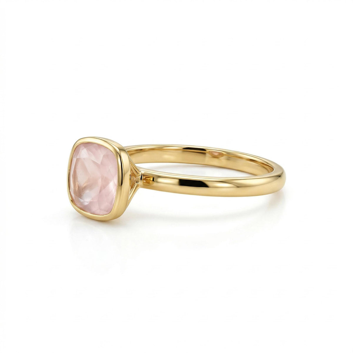 A side profile view of a gold bezel-set ring with a cushion-cut pale pink stone on a white background.