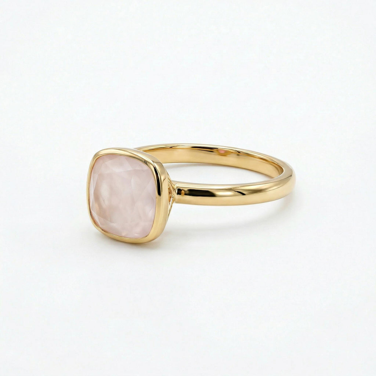 A close-up three-quarter view of a gold ring with a faceted cushion-cut pink gemstone.