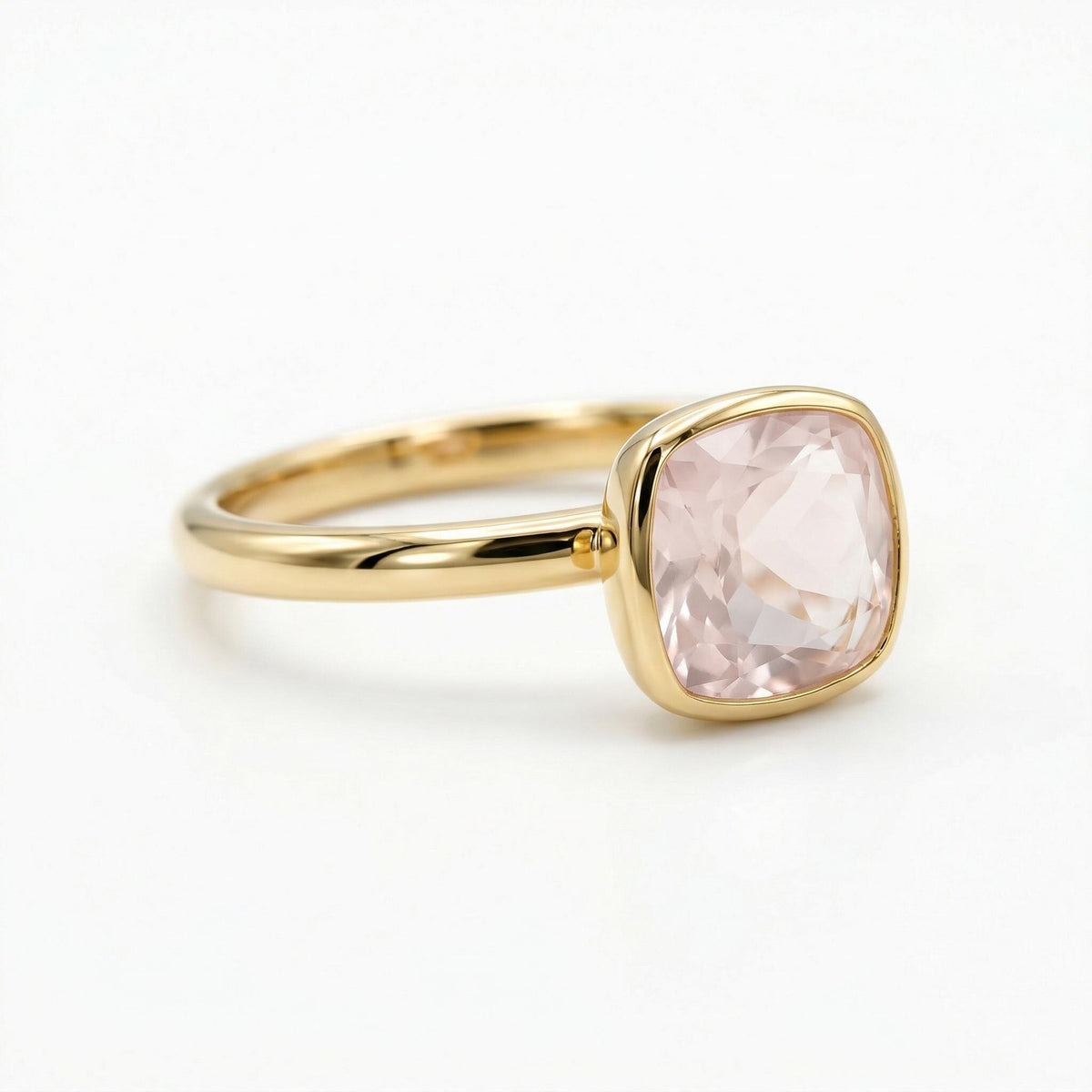 An angled studio shot of a gold ring holding a square faceted pink gemstone with rounded corners.