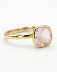 An angled studio shot of a gold ring holding a square faceted pink gemstone with rounded corners.
