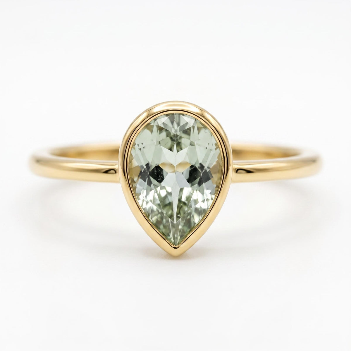 Front-facing studio shot of a pear-shaped light green tourmaline gemstone in a yellow gold bezel setting on a thin gold band against a plain white background.