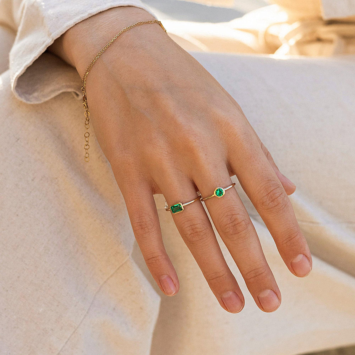 A hand wears two gold rings featuring rectangular green gemstones set horizontally on the fingers.