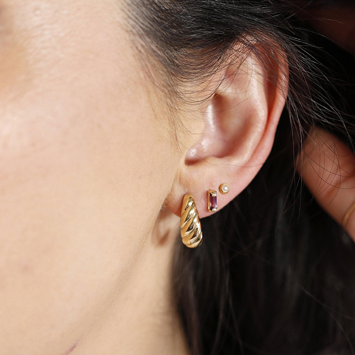 A close-up of a person's ear wearing a gold croissant hoop earring in the first lobe piercing.