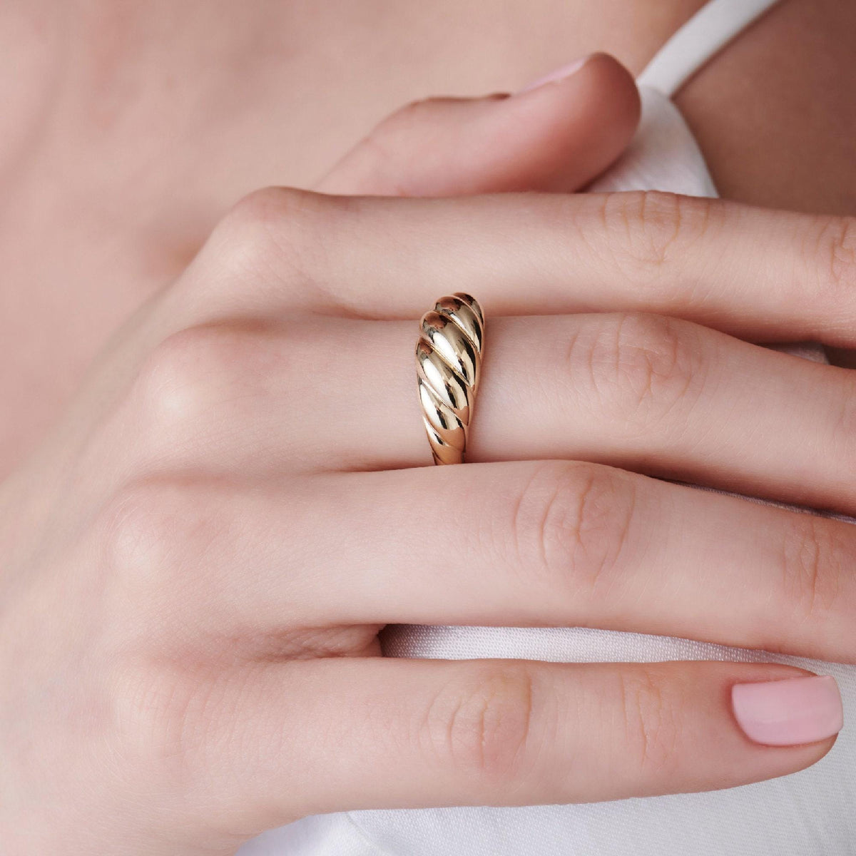 A close-up of a person wearing a gold ribbed dome ring on their ring finger.