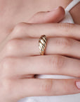 A close-up of a person wearing a gold ribbed dome ring on their ring finger.