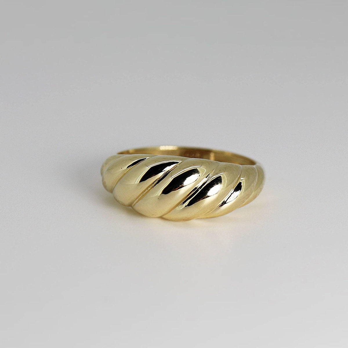 A gold croissant-style ring isolated on a light gray surface.