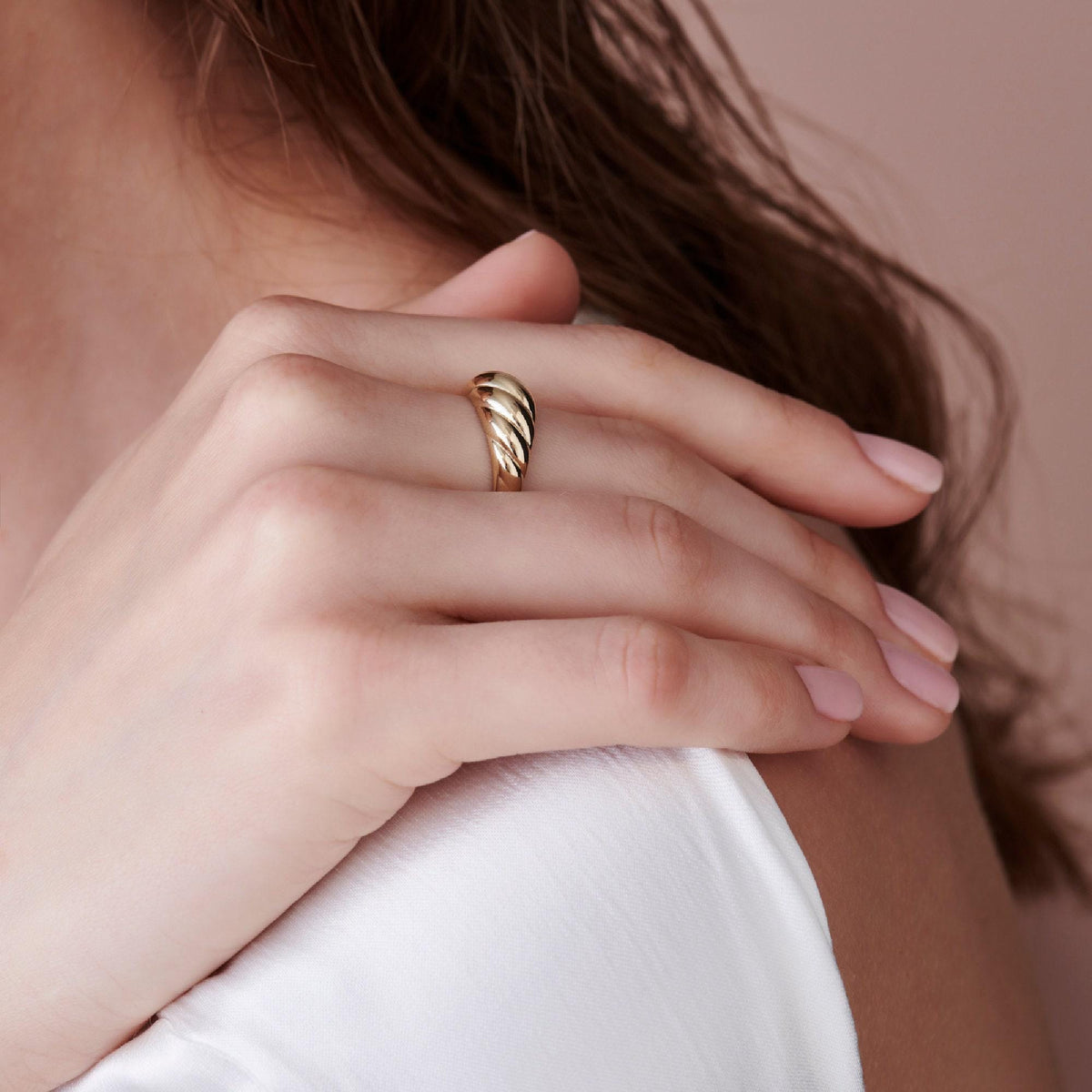 A side view of a person resting their hand against their shoulder, wearing a gold twisted ring.
