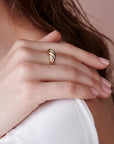 A side view of a person resting their hand against their shoulder, wearing a gold twisted ring.
