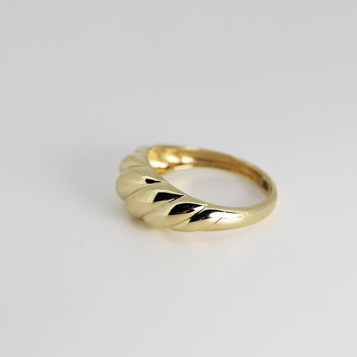 A single gold ribbed dome ring photographed at an angle on a plain white background.