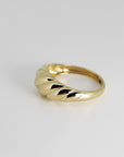 A single gold ribbed dome ring photographed at an angle on a plain white background.