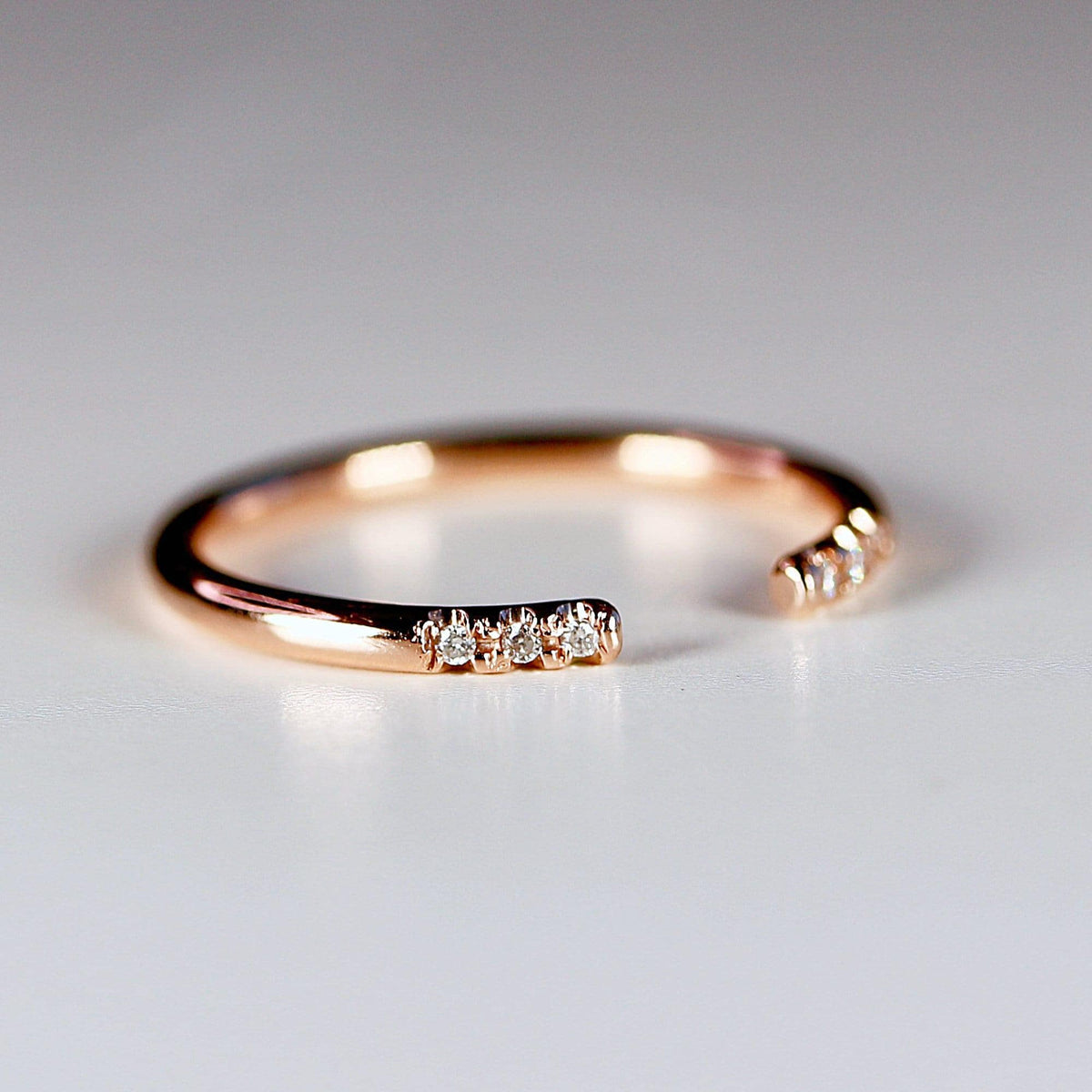 A macro shot of a rose gold open cuff ring resting on a surface, highlighting the small diamonds.