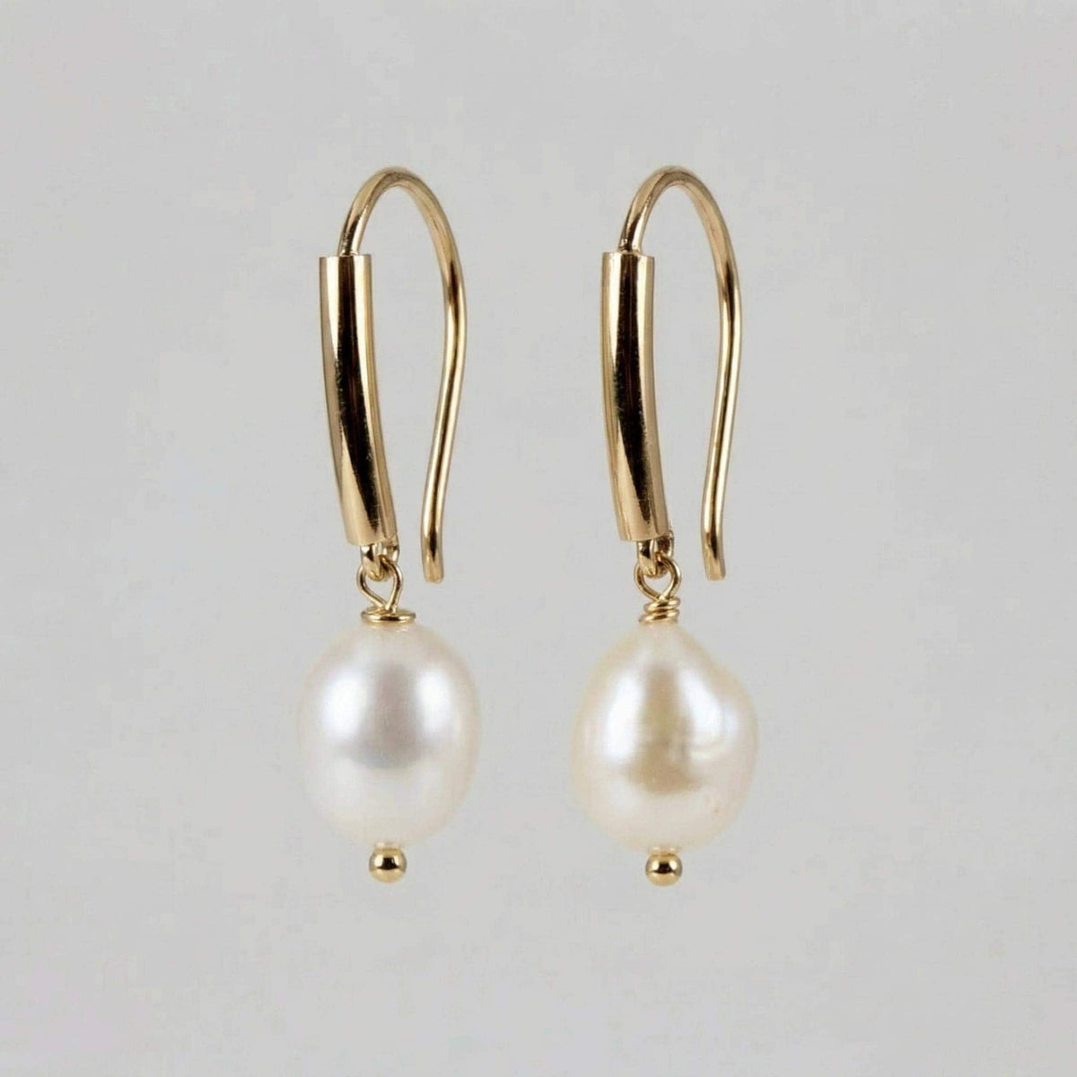 A straight-on view of the gold-filled and white baroque pearl dangle earrings lying flat against a neutral light background.