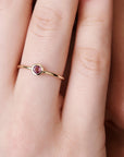 Close-up of a hand wearing a thin gold ring with a bezel-set pink gemstone.