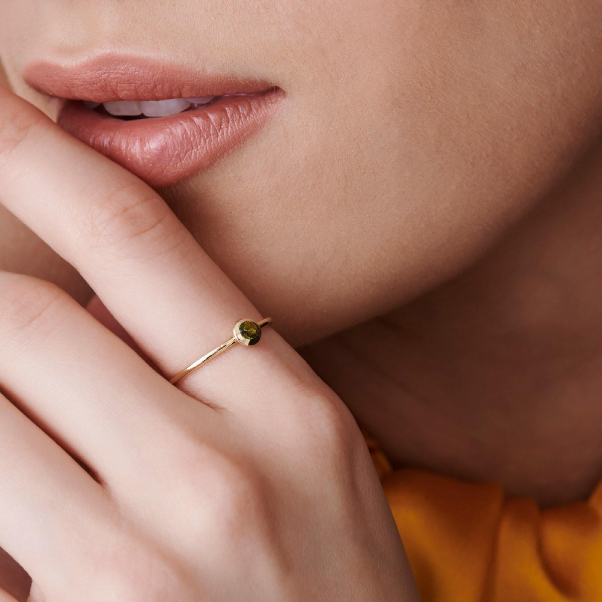 Close-up of the lower face of a person wearing a thin gold ring with a green gemstone near their lips.