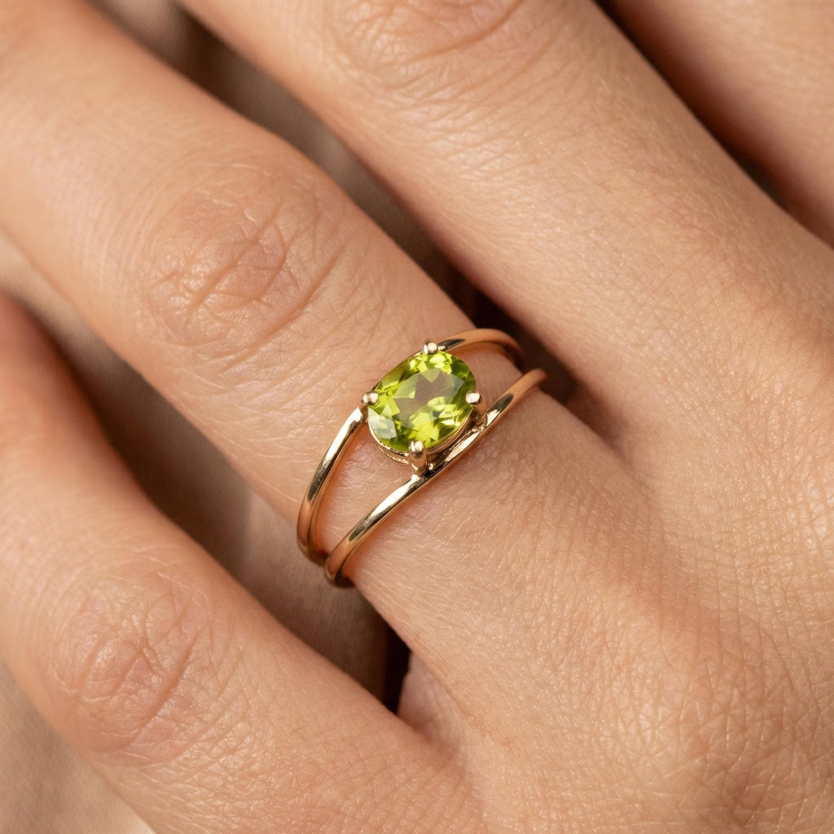 The gold double-band peridot ring is worn on a finger against a neutral fabric background.