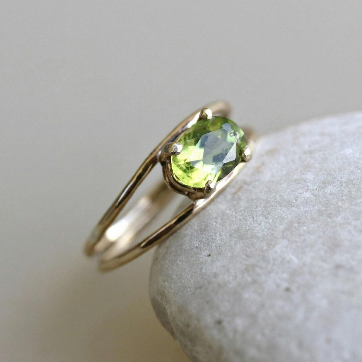 The gold and peridot double-band ring rests on top of a light-colored smooth stone.