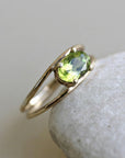 The gold and peridot double-band ring rests on top of a light-colored smooth stone.