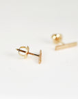 A gold bar stud earring displays its threaded post and screw back mechanism on a white surface.