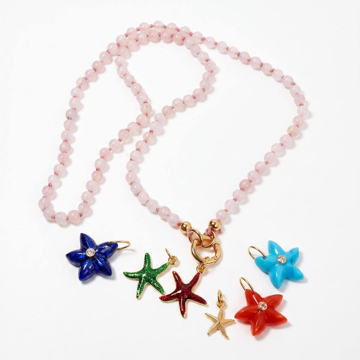 A light pink gemstone bead necklace laid out on a white surface with a gold clasp and several colorful starfish charms arranged below it.