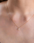 A person wearing a dark top showcases a delicate gold chain necklace with a small heart gemstone pendant.