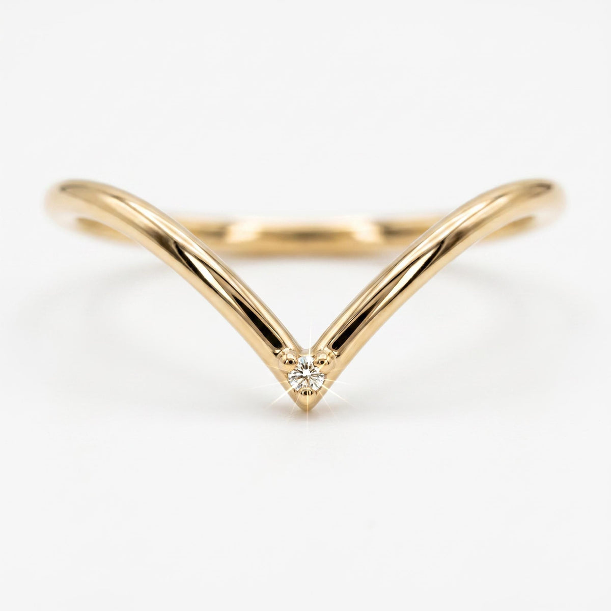 A thin, polished gold chevron ring features a single small round gemstone set at the centered point against a plain white background.