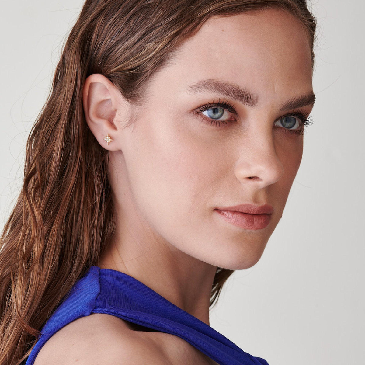 Medium close-up of the model wearing the small gold star stud earring, angled slightly further away against a plain light background.