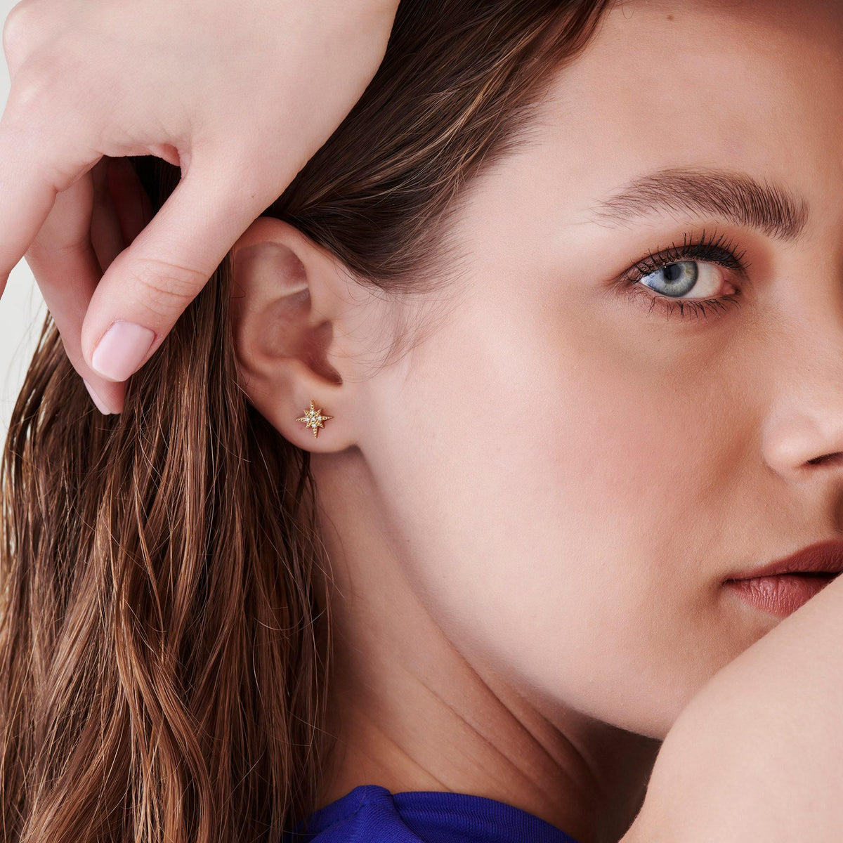 Tight shot focusing on the ear wearing the gold starburst stud earring while a hand with pale pink polished nails rests near the hair.
