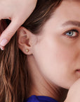 Tight shot focusing on the ear wearing the gold starburst stud earring while a hand with pale pink polished nails rests near the hair.