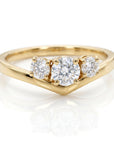 A yellow gold three-stone ring with a V-shaped chevron band rests on a white surface, displaying a large center diamond and two smaller side diamonds.