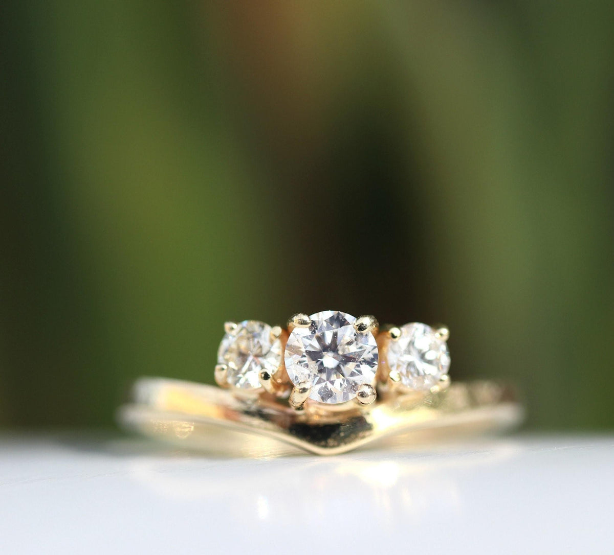 Macro shot of the gold three-stone diamond ring with a blurred natural green background.