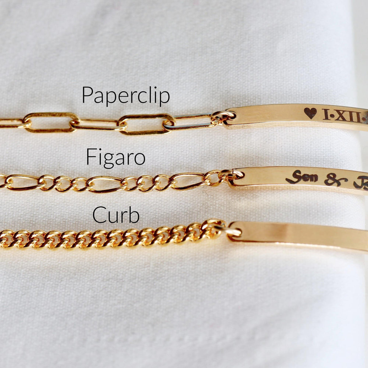 Three gold bracelets with different chain styles labeled Paperclip, Figaro, and Curb attached to engraved bar pendants.