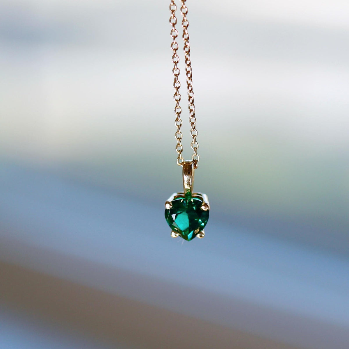 Macro shot of a faceted green heart pendant on a thin gold chain against a blurred background.
