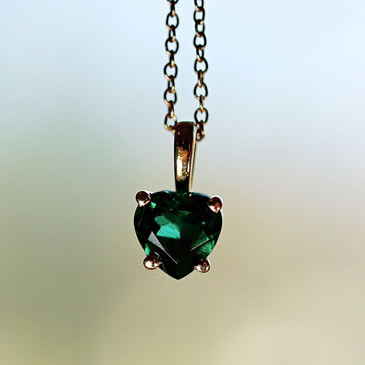 Detailed close-up of a green heart gemstone held in a four-prong gold pendant setting on a chain.