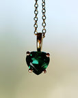 Detailed close-up of a green heart gemstone held in a four-prong gold pendant setting on a chain.