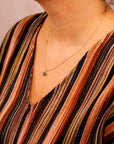 A person wearing a multicolored striped top wears a gold chain necklace with a green heart pendant.