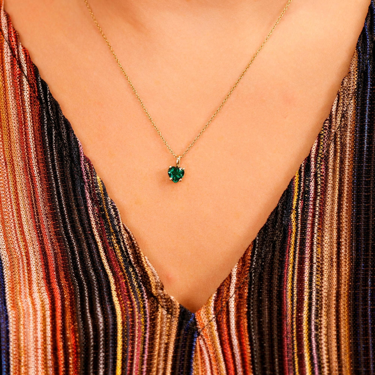 Close-up of a small green heart-shaped pendant on a gold chain worn against a striped top.