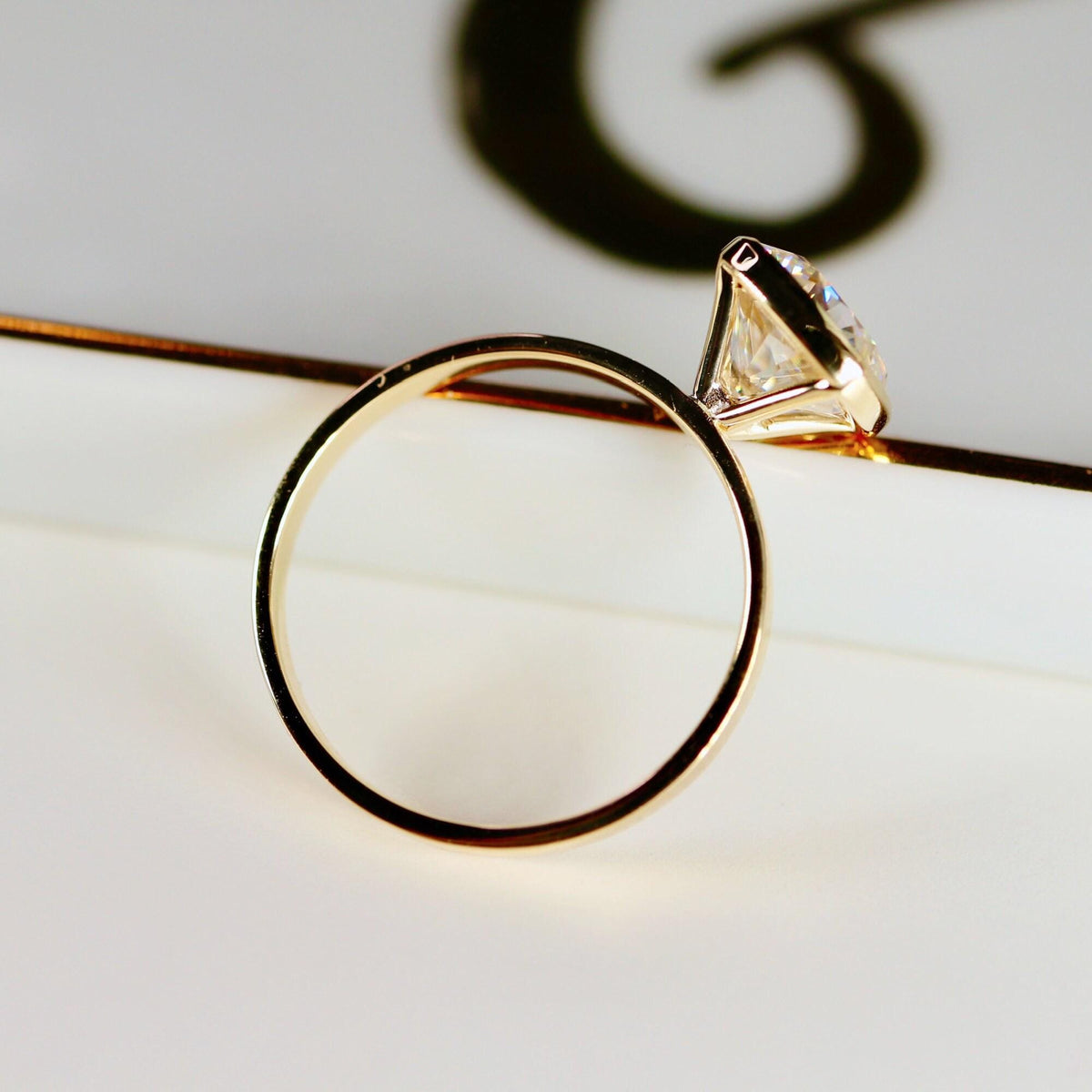 Angle view of the gold bezel-set cushion cut ring showing the inside of the circular band.