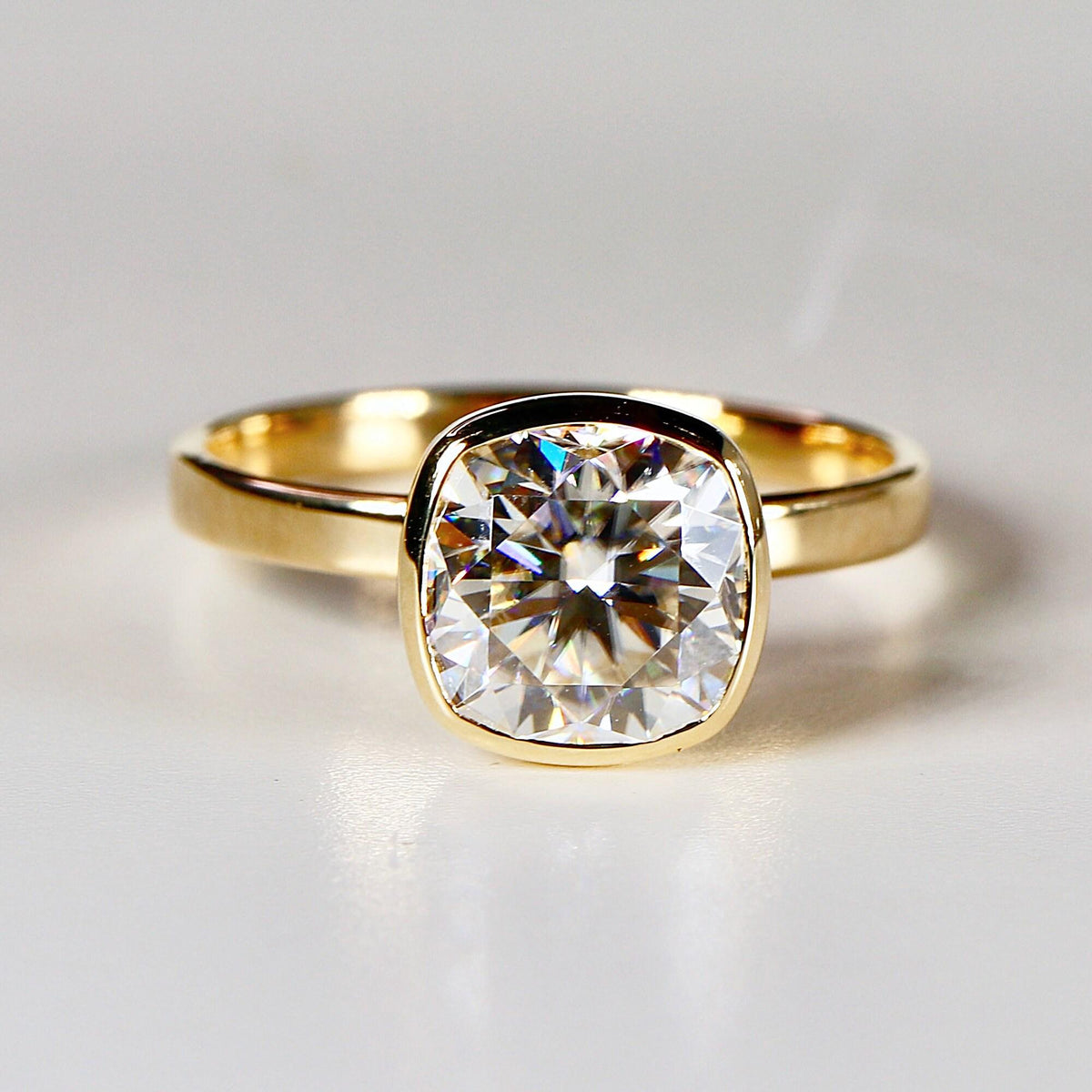 Front-facing close-up of a gold ring featuring a large, faceted cushion cut stone in a bezel setting.
