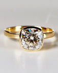 Front-facing close-up of a gold ring featuring a large, faceted cushion cut stone in a bezel setting.