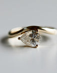 A close-up studio shot of a gold ring featuring a pear-shaped gemstone held by three prongs on a wavy band.