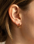 A close-up side profile of a person wearing a gold hoop earring set with three red stones in the earlobe.