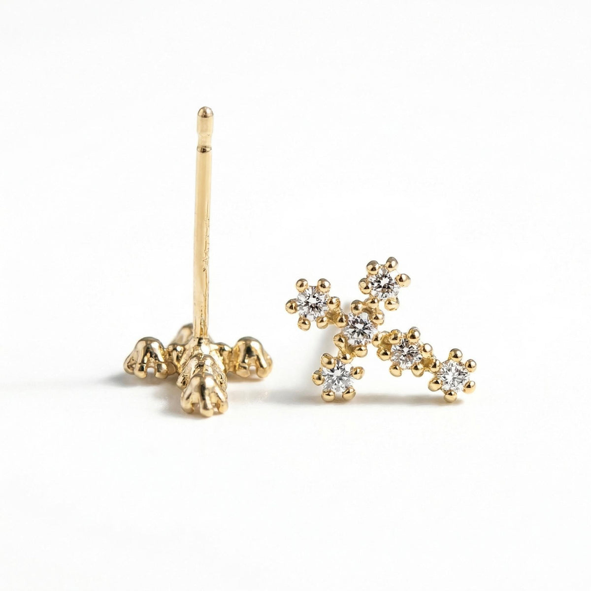 Two gold cross stud earrings shown with one standing upright on its post on a white surface.