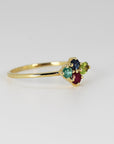 Side view of a gold cluster ring featuring red, blue, green, and light green gemstones resting on a white surface.