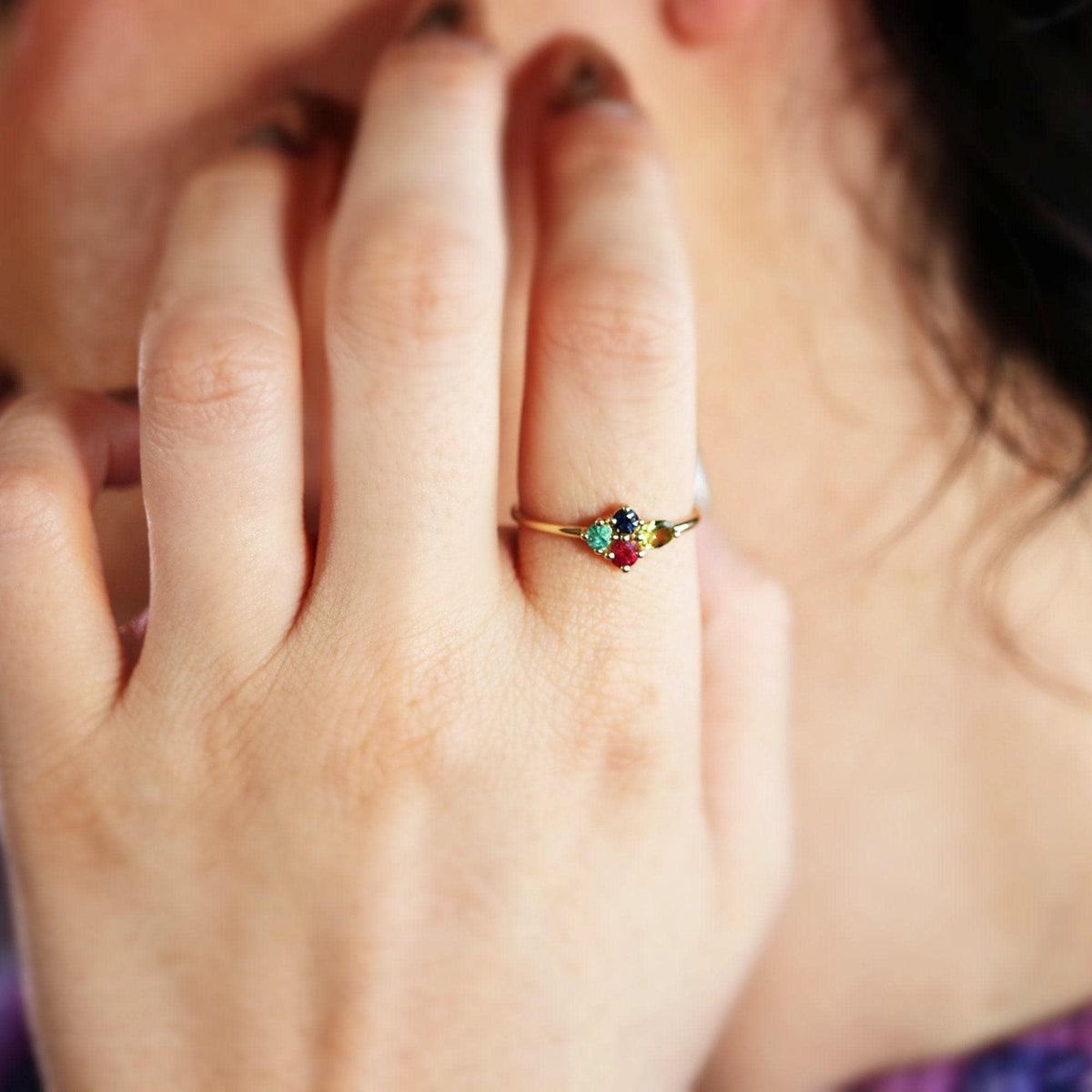 Close-up of a hand with a colorful multi-stone gold ring on the ring finger.