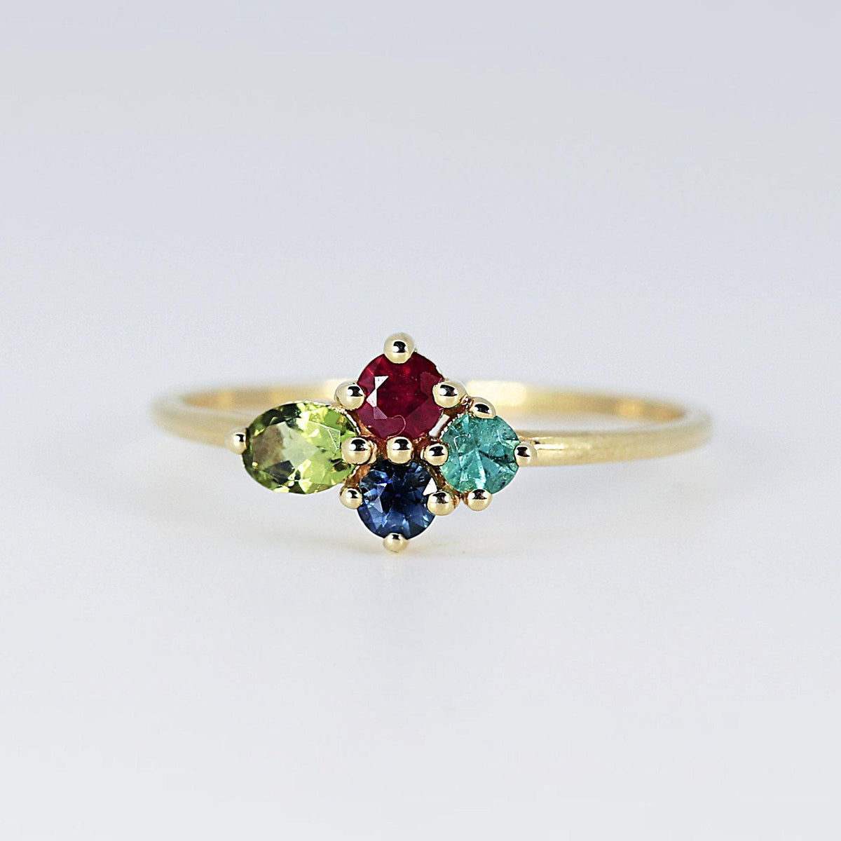 Front view of a gold ring featuring a cluster of four colorful faceted gemstones against a neutral background.