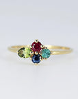 Front view of a gold ring featuring a cluster of four colorful faceted gemstones against a neutral background.