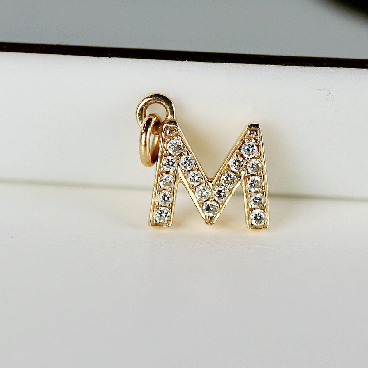 A close-up of a gold letter M charm embedded with small diamonds.