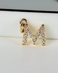 A close-up of a gold letter M charm embedded with small diamonds.